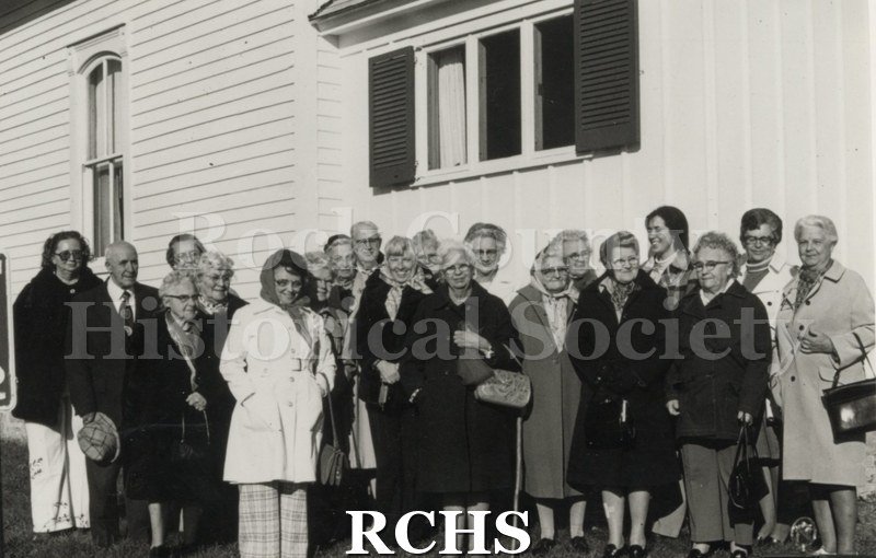 Black and white photograph of Rock County Historians, Avon Church. Shows several women and men standing beside a building. They are wearing winter clothes.