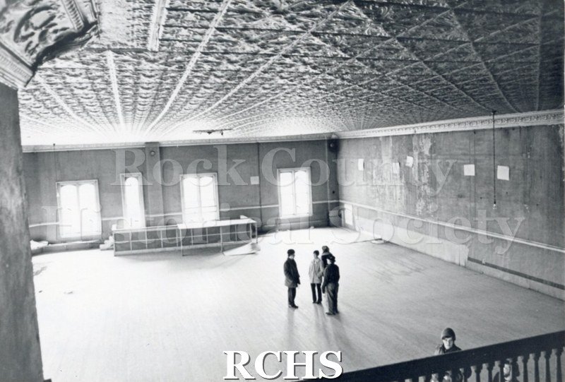 Black and white photograph of Myers Block-Old Armory, Janesville, WI, interior view, showing the ceiling in detail. Five people are visible in the frame.