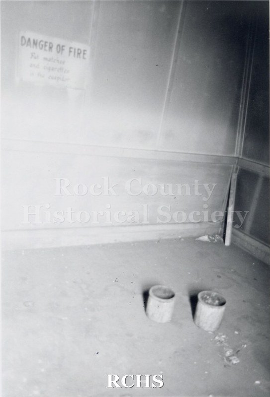 Black and white photograph of Myers Block-Old Armory, Janesville, WI, interior view, showing a wall with a sign: "Danger of Fire" on it and two pails on the floor.