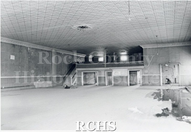 Black and white photograph of Myers Block-Old Armory, Janesville, WI, interior view, showing a stairway up to the balcony.