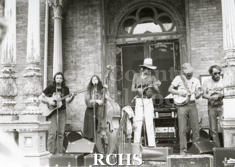 Black and white photograph of the Tallman Arts Exhibit. A band is performing on the porch of the Tallman House.