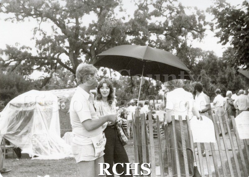 Black and white photograph of the Tallman Arts Exhibit. People are strolling along the sidewalk in front of the Tallman House at the ticket stand.