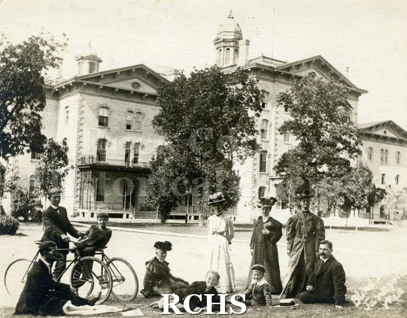 Black and white photograph of the Wisconsin School for the Visually Handicapped, Janesville, WI, showing ten people sitting and standing in front of it.