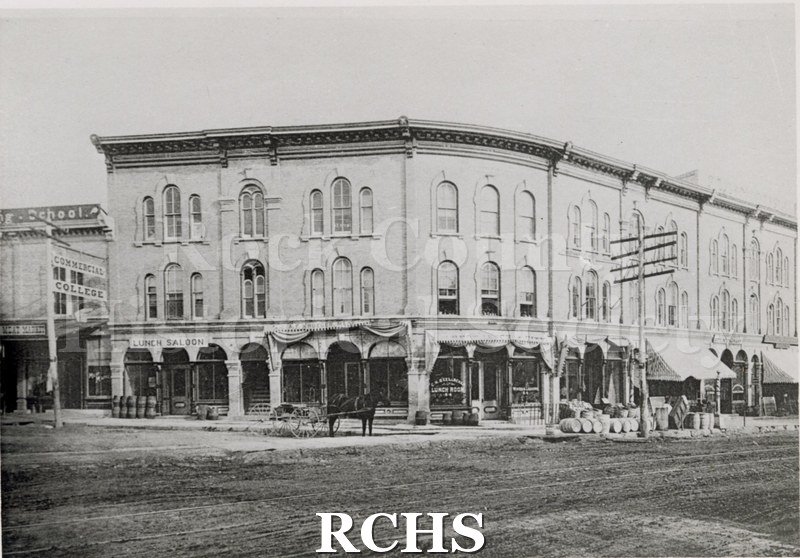 Black and white photograph of Corn Exchange, Janesville, WI, an intersection in Janesville. Shows a large three story building with arched windows.