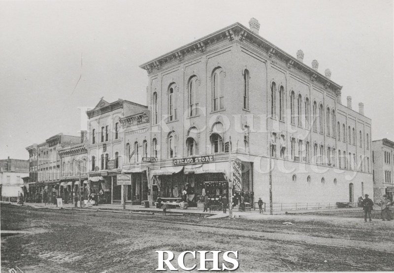 Black and white photograph of the SE corner W.Milwaukee/River, Janesville, W. Shows a corner building with a sign: "Chicago Store" above the canopy.