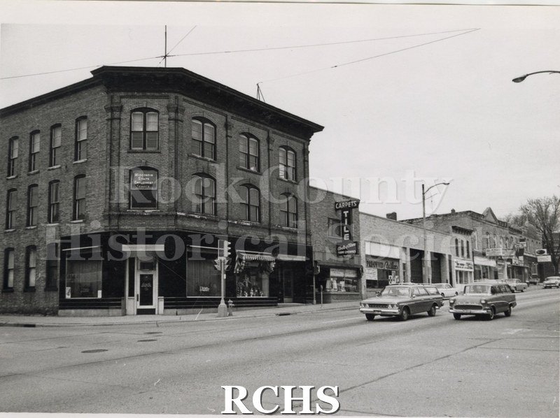 Black and white photograph of Early Milwaukee Street. Shows a corner building with the Wisconsin State Employment Services in the second floor window.