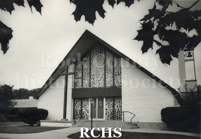 Black and white photograph of St. Mary Catholic Church-Milton, a church with a stained glass doorway. The stained glass windows go up to the rooftop.