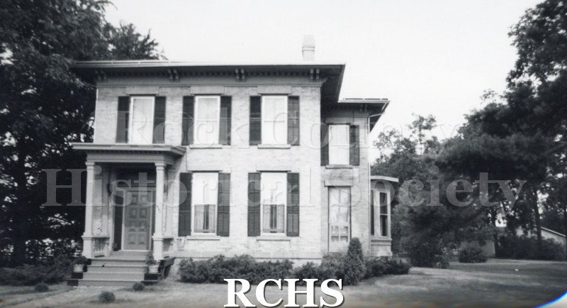 Black and white photograph of an unidentified two story house with symmetrical windows. There is a pillared porch on the left side.