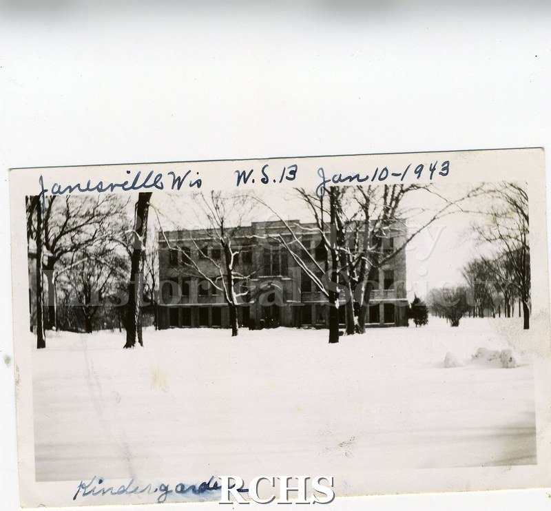 Black and white photograph of the Wisconsin School for the Blind, Kindergarten, is a three story building standing alone. There is snow on the ground.