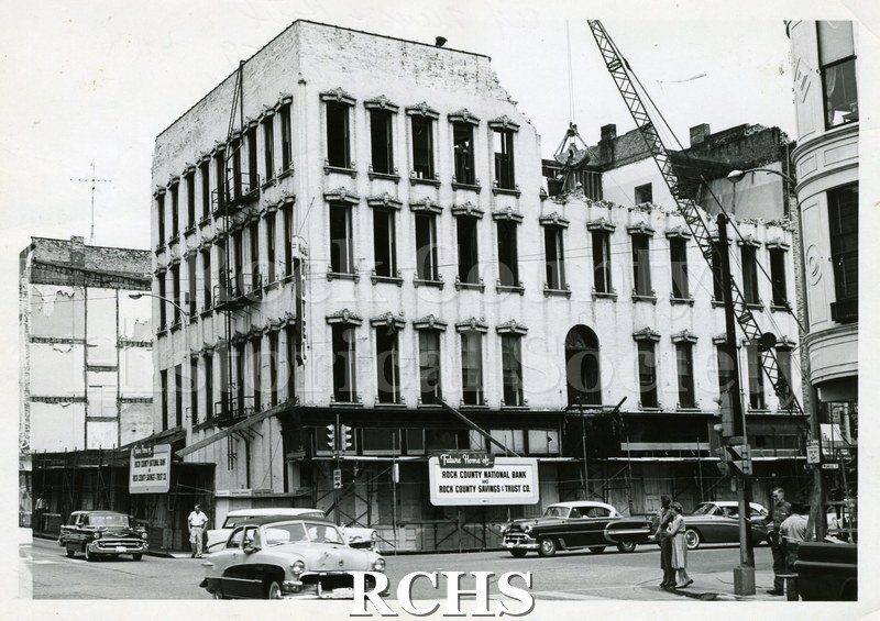 Black and white photograph of the Myers Hotel Demolition. There is a crane on the right side of the street and barricades on the sidewalk in front of the building.
