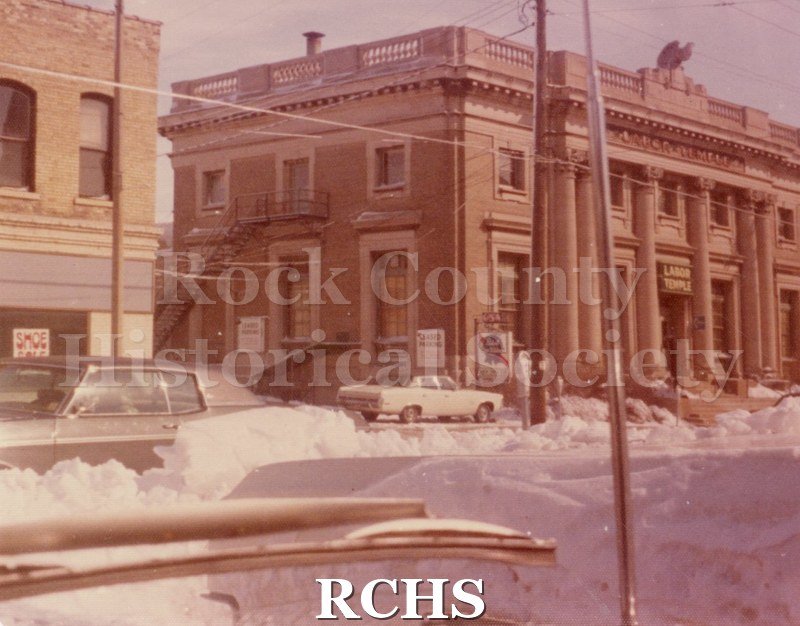 Color photo of the Janesville Post Office. Shows a two story building with a balustrade on top. A ceramic eagle is perched on top of it.