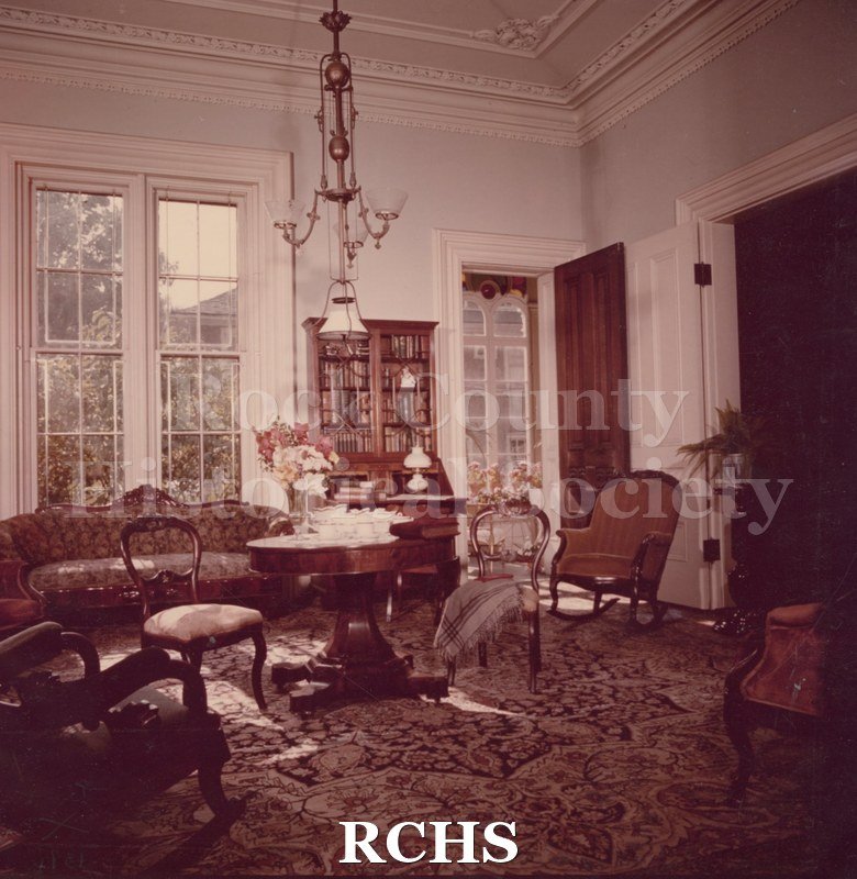 Color photo of the Library of the Tallman House. Shows a round table set with dishes and two chairs beside it.