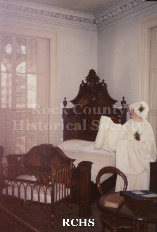 Color photo of an unidentified person dressed in white in a bedroom of the Tallman House.