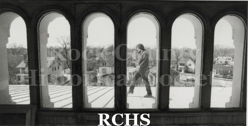 Black and white photograph of an unidentified man walking in the observatory, framed by six arched windows.
