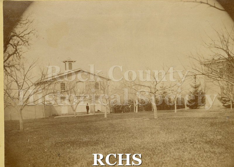 Sepia photo of the Carriage house on the Tallman property. There is a man standing in front of the barn and a horse and buggy on the driveway. .