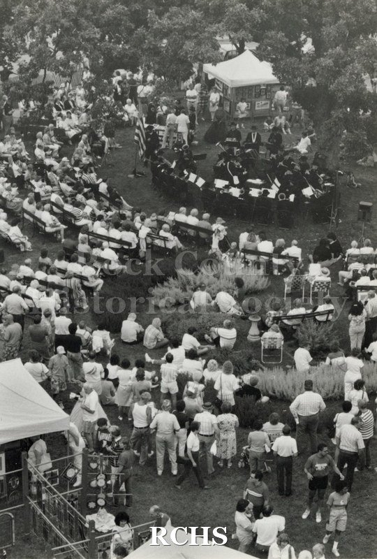 Black and white photograph of aerial photograph of people at the Arts Festival. In the background the Civil War era band is performing.