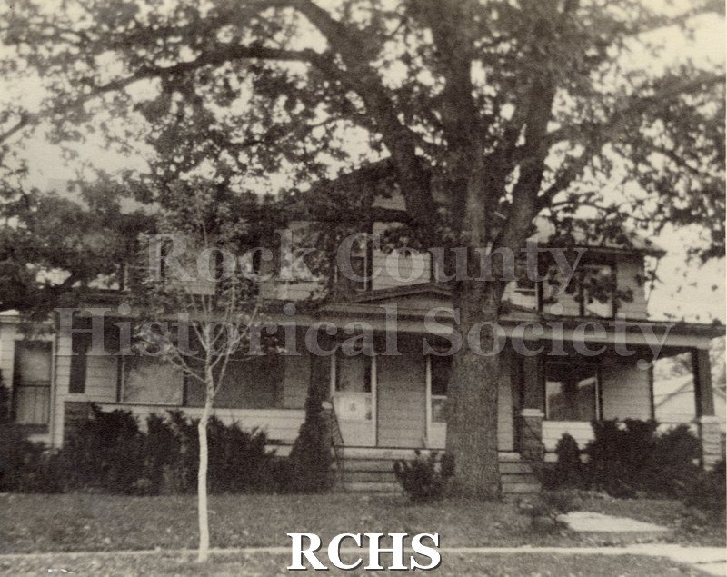 Black and white photograph of Rhoda Lavinia Goodell's home, a two story house with double doors and a porch along the front of the house.