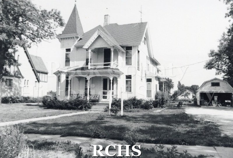Black and white photograph of an unidentified three story house with a pillared porch and a covered balcony on top. There is a tower on the left side.
