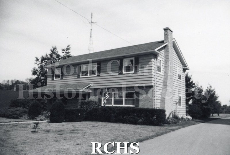 Black and white photograph of an unidentified two story house with a chimney on the right side and an American flag in the front.