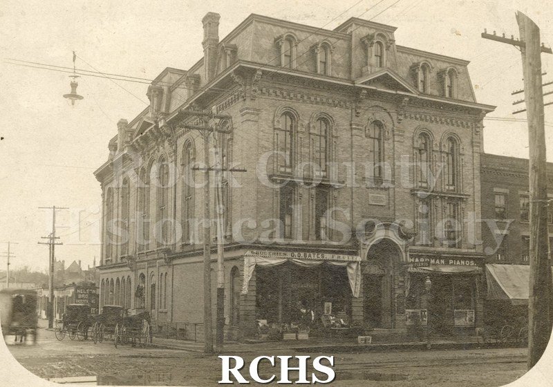 Tinted photo of a four story building with O.D. Bates Groceries and fruits on the left first floor and Hardman Pianos on the right first floor.