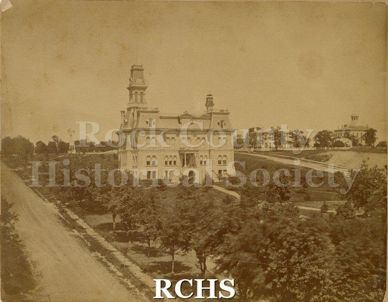 Sepia photo of the Rock County Courthouse surrounded by trees. On bottom: "Photo by A. Morse & Corp, Milwaukee, Wis.".