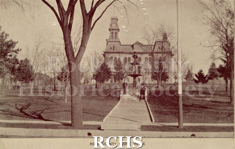 Black and white photograph of the Rock County Court House. There are two men standing on the steps by the lamppost.