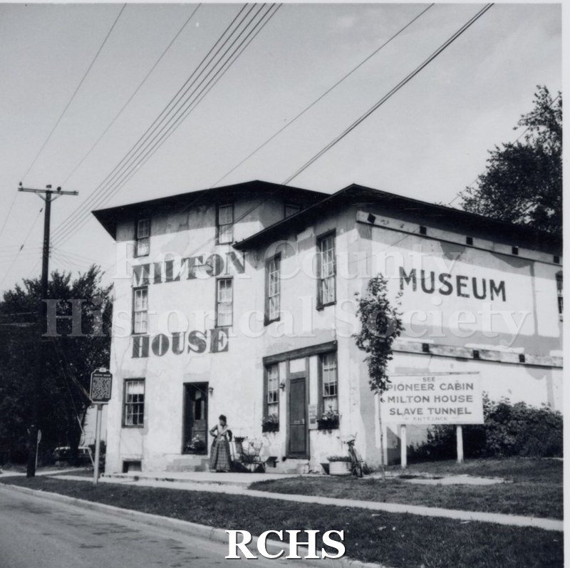 Black and white photograph of the Milton House Museum. Shows a sign: "See Pioneer Cabin, Milton House, Slave Tunnel".