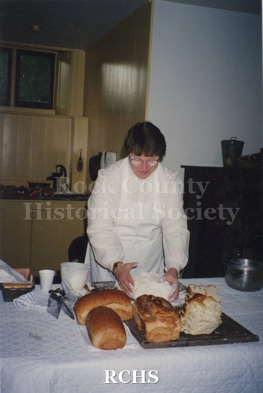 Color photo of Judy Armstrong demonstrating bread making. She has several finished loaves in front of her and is shaping another one.