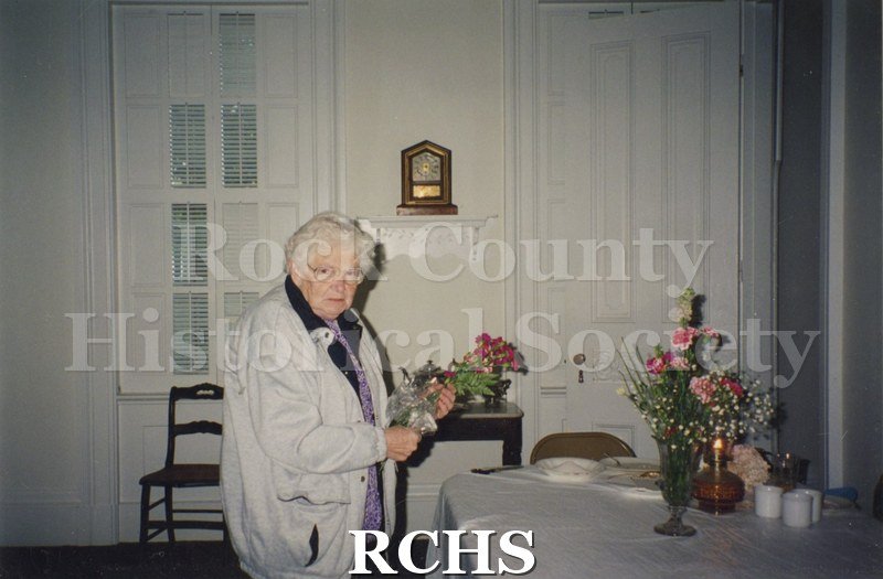 Color photo of Nell McGinnis with a bouquet of flowers in her hand. Other arrangements are on the table in front of her.
