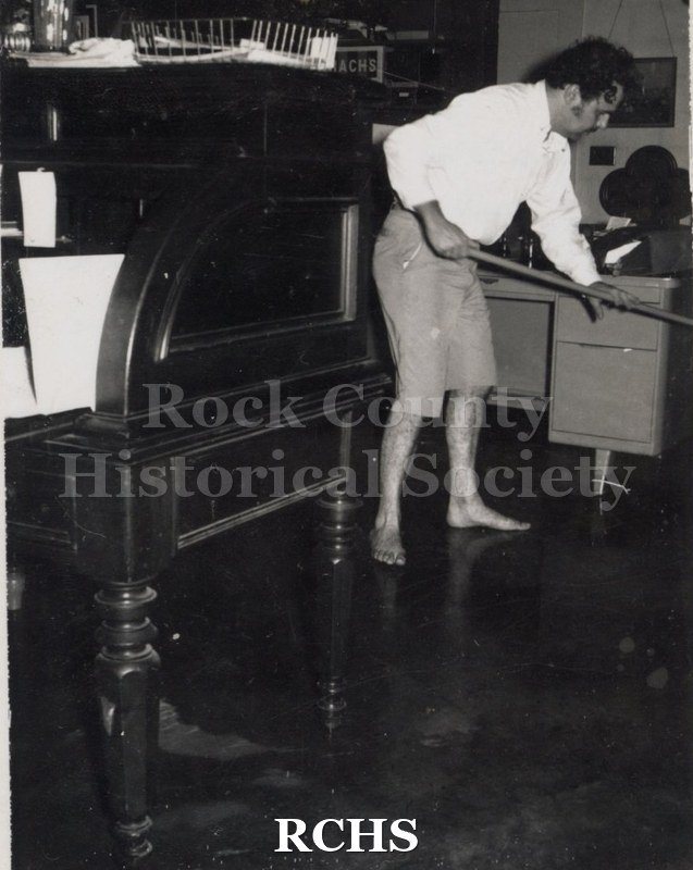 Black and white photograph of Richard Hartung in bare feet mopping a floor.