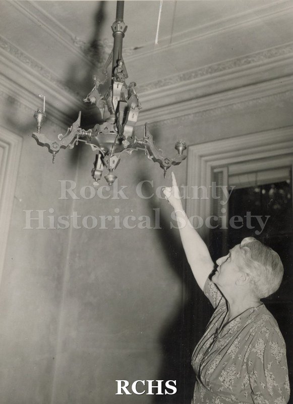 Black and white photograph of Mrs. G. K. Tallman pointing to a gas light fixture in the Tallman House.