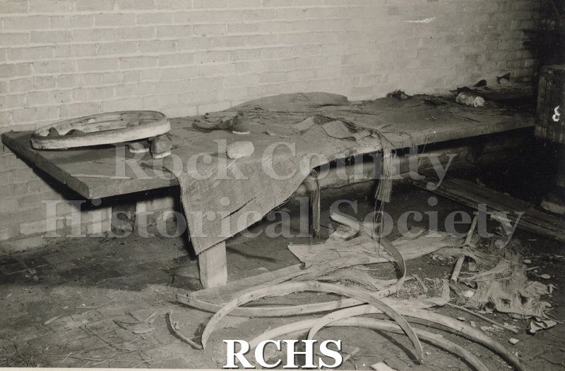 Black and white photograph of benches along the wall in the Talllman House. There is debris in front of them.