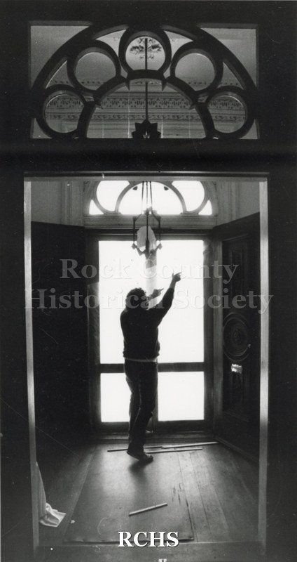 Black and white photograph of an unidentified man holding something in his hand while standing at the window.