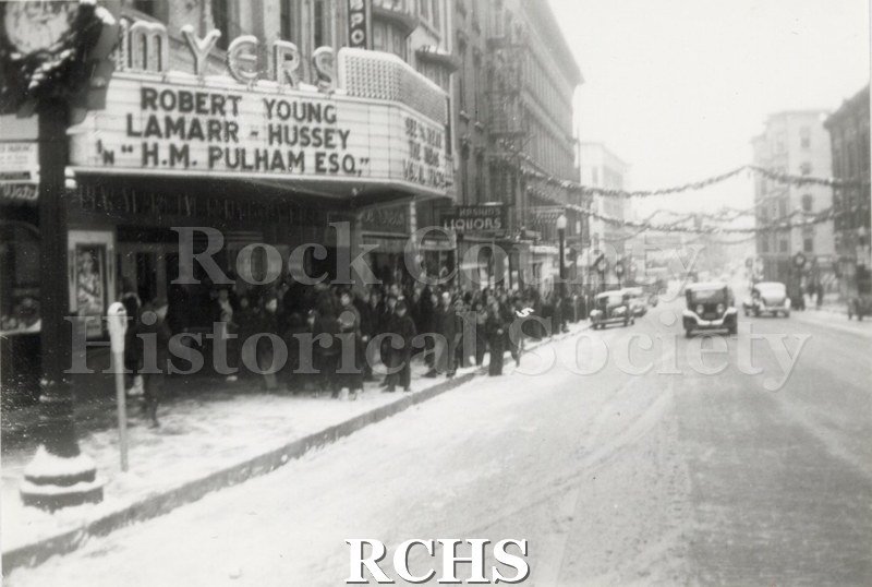 Black and white photograph of East Milwaukee Street in downtown Janesville with Christmas decorations strung across the street and on lampposts.