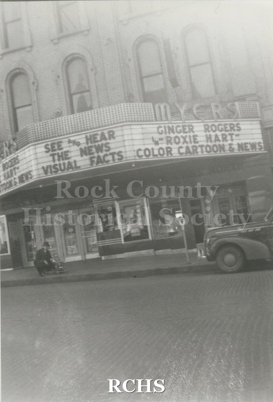 Black and white photograph of Clyde Haney and Richard Haney at the Myers Theater near the marquee. It features Ginger Rogers in "Roxie Hart" Color Cartoon & News.".