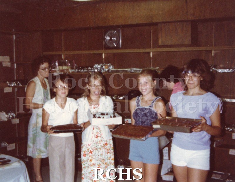 Color photo of six women volunteers. Four of them are holding cakes.