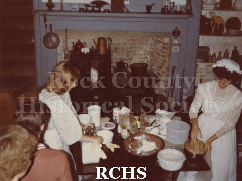 Color photo of June and Kim Loper demonstrating bread making and butter churning in the kitchen at the Tallman House.