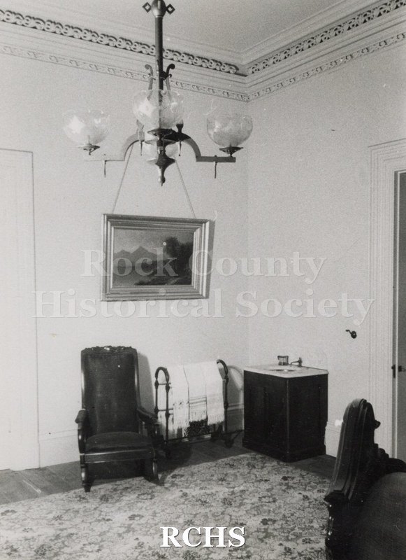 Black and white photograph of the Lincoln bedroom in the Tallman House showing a chair on the left, a towel rack with towels on it, and a marble sink with one.