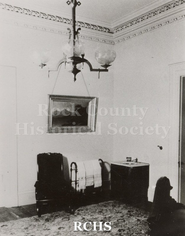 Black and white photograph of the Lincoln bedroom in the Tallman House showing a chair on the left, a towel rack with towels on it, and a marble sink with one.
