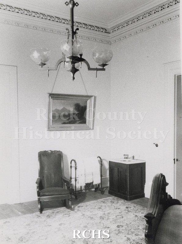 Black and white photograph of the Lincoln bedroom in the Tallman House showing a chair on the left, a towel rack with towels on it, and a marble sink with one.