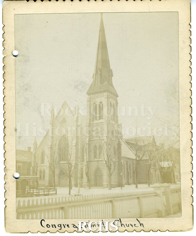 Blackand white photograph of the Congregational Church, Janesville, WI. It has a three story bell tower and a fence in front..