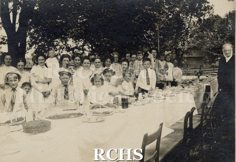 Black and white photograph of Shopiere Congregational Church Anniversary. Shows people standing behind tables filled with food.