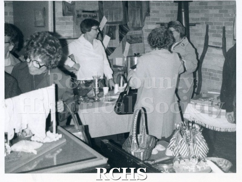Black and white photograph of the Christmas Boutique. Women are standing around various tables with items on them.