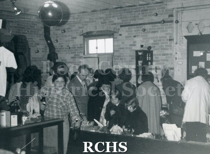 Black and white photograph of the Christmas Boutique. Men and women are looking over exhibits.