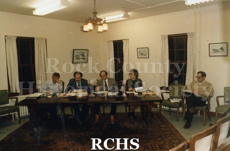 Color photo of the RCHS Board of Trustees meeting 1982. Four people are sitting at a table and another is sitting on a chair on the right.