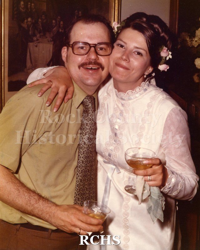 Color photo of an unidentified couple holding champaign glasses. The woman has her arm around the man.