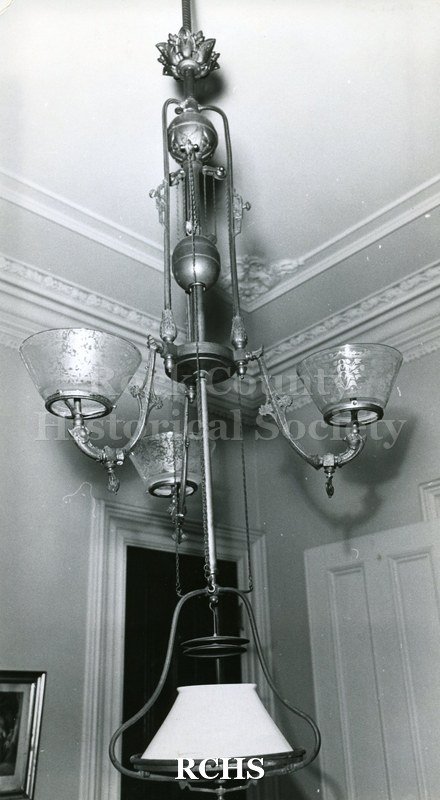 Historic image of Tallman House chandelier. It has three glass bowls in the middle and a bell-shaped white inverted bowl at the bottom.