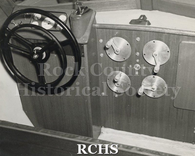 Black and white photograph of "High Pockets" on a hoist at naval yard. Shows the cockpit of the boat with the wheel and other gauges.