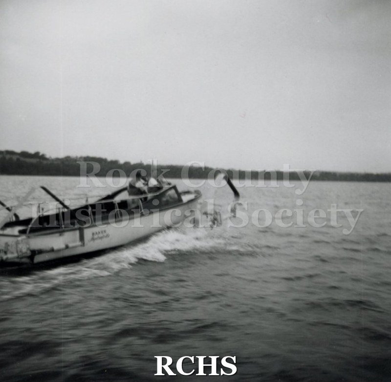 Black and white photograph of "High Pockets" moving through the water with two men aboard. The name: "Baker ____" is visible on the side. "13".