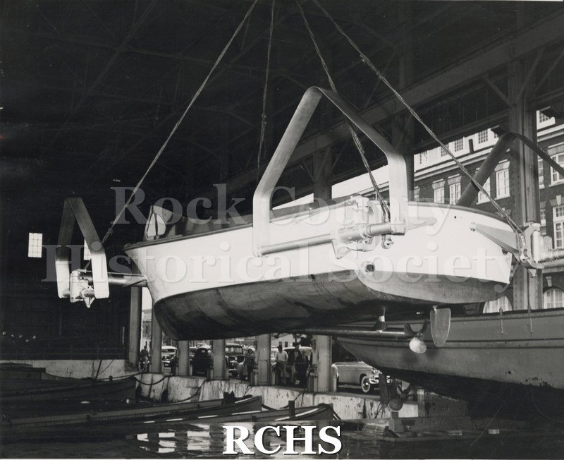Black and white photograph of "High Pockets" on a hoist at naval yard with another naval vessel below it.